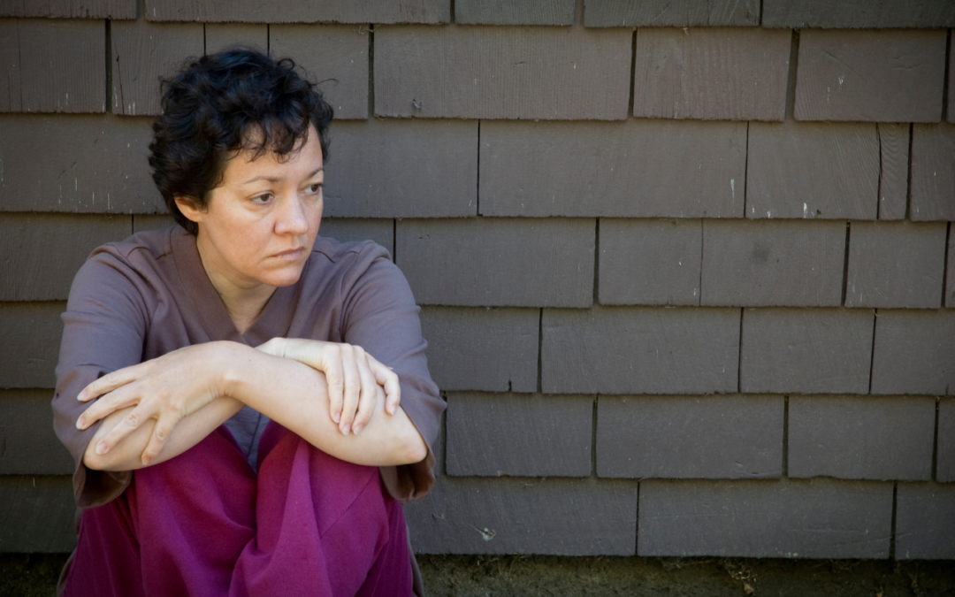 Woman sits against dreary grey brick wall, despondent