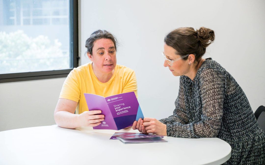 Woman wearing yellow tshirt reads Sharing your experience brochure with support from woman wearing glasses